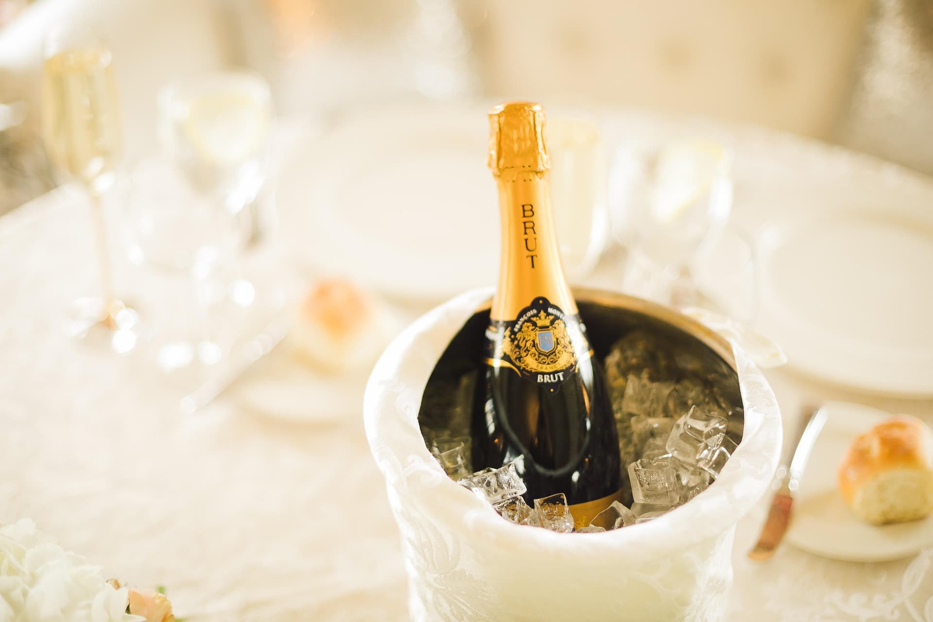 Bouteille de champagne dorée dans un seau à glace, décor blanc, arrière-plan lumineux et flou.
