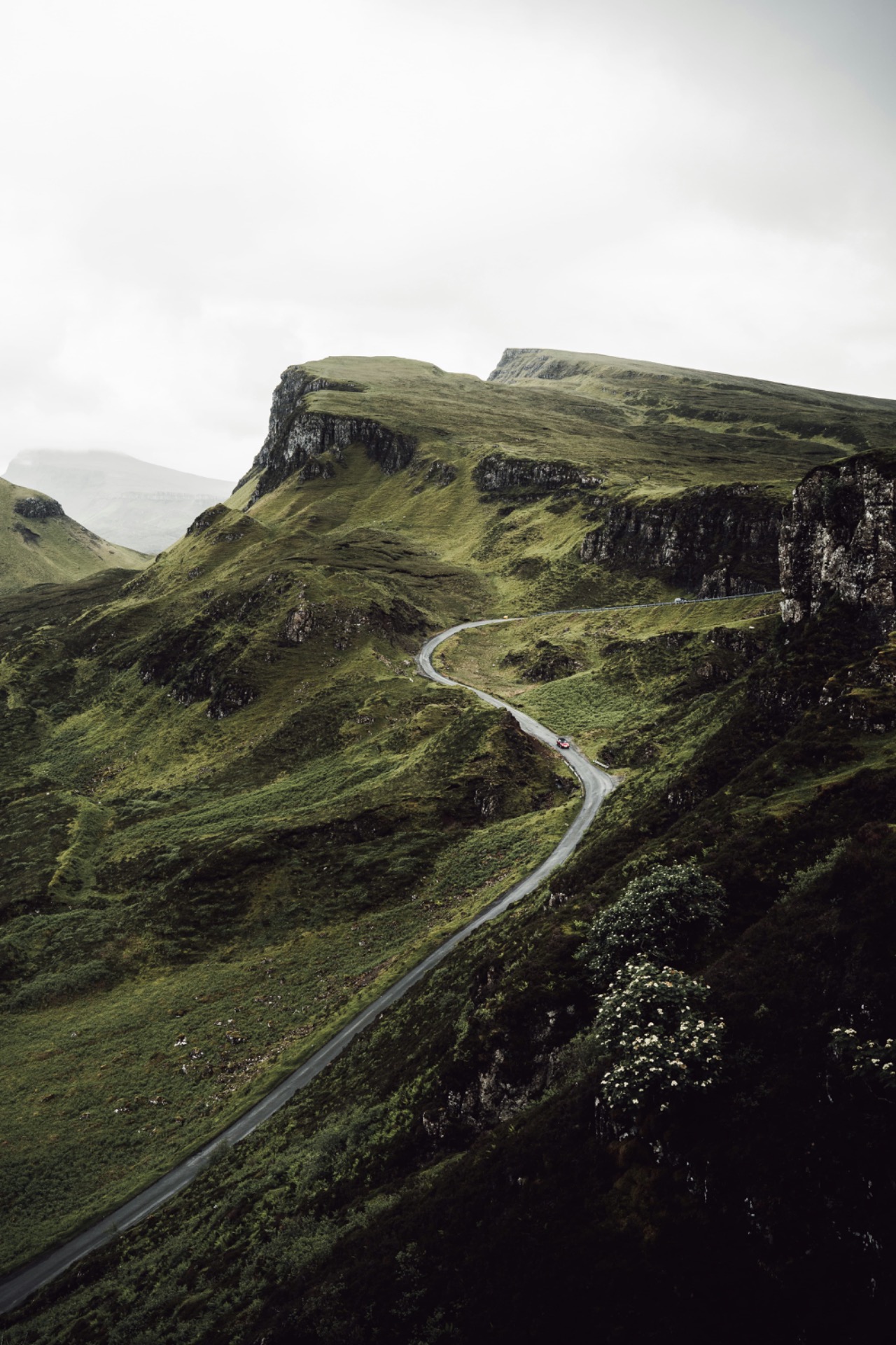 Route sinueuse traversant des collines verdoyantes et falaises rocheuses sous un ciel gris, en Irlande.